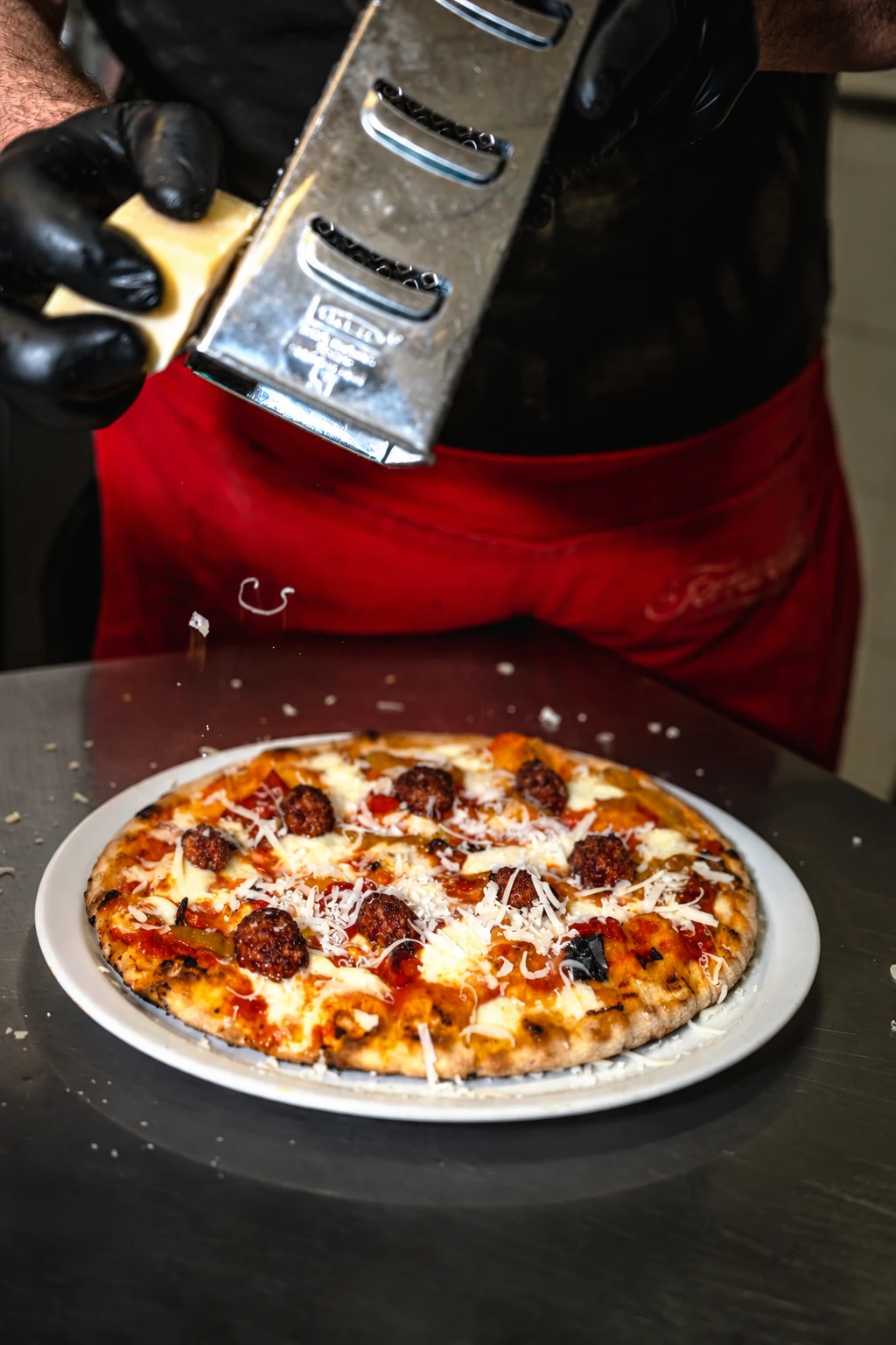 Il pizzaiolo grattugia il formaggio su una pizza tonda appena preparata